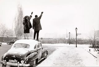 Lon Herschtritt : "Nol  Berlin. A l'angle d'une rue enneige depuis Bergtrasse, un couple debout sur le toit d'une voiture lve le bras pour saluer de l'autre ct du mur vers Berlin Est" 1961 (c) Paris, Muse de l'Arme/Emilie Cambier/Lon Herschtritt